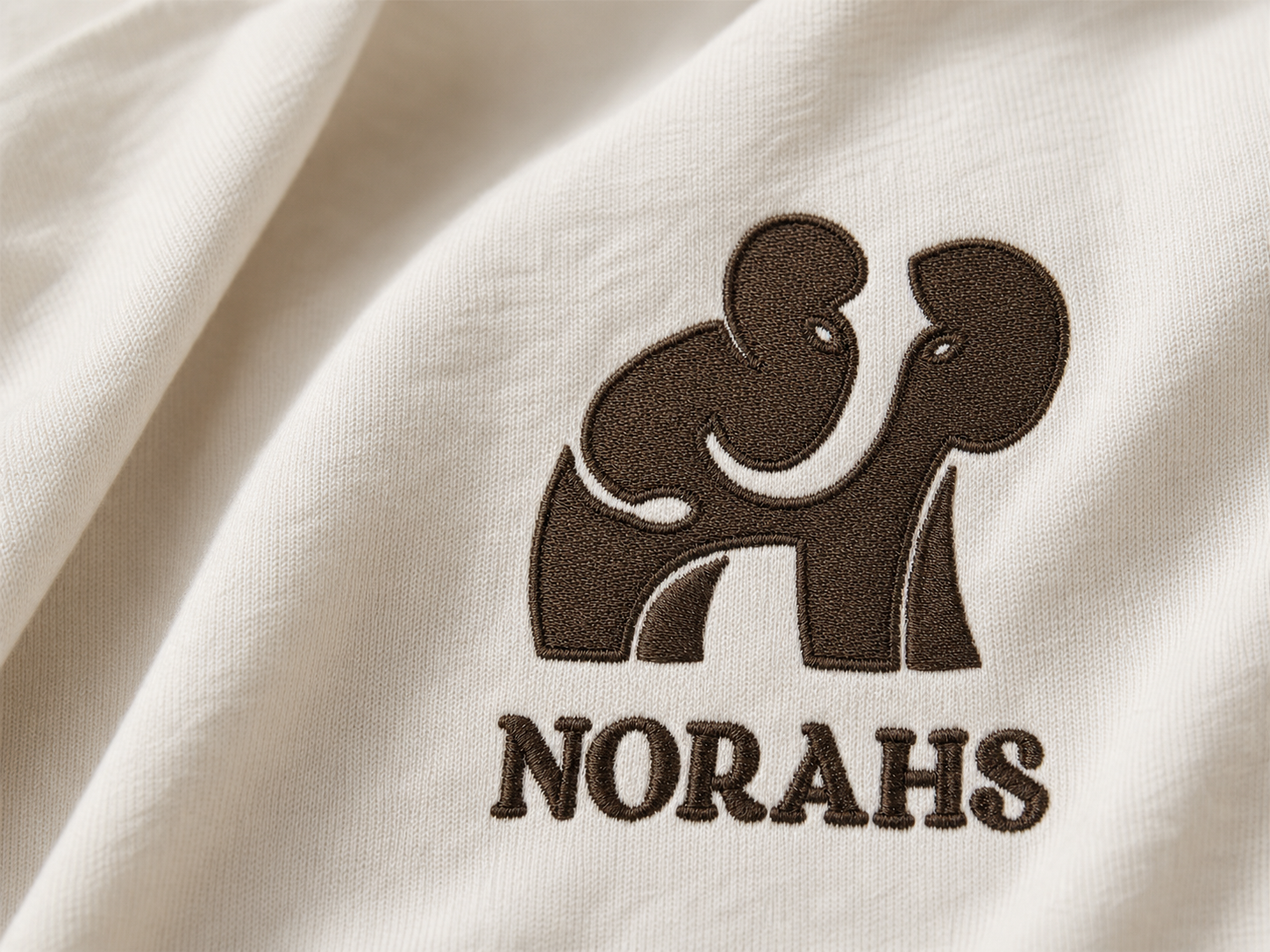Close-up of dark-brown Norahs elephant embroidery on natural cotton